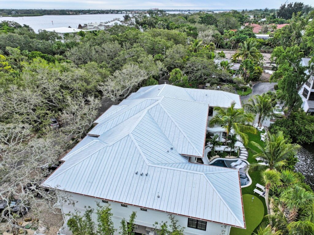 High-angle bird's-eye perspective of a sweeping waterfront estate featuring a bright silver corrugated system, illustrating durable Metal Roofing Types from Sunshine Metal Supply.