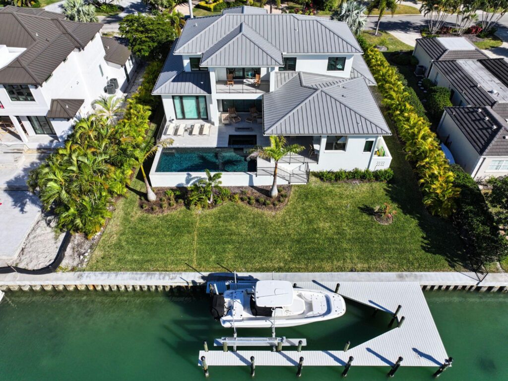 Overhead view of a luxury modern coastal mansion with a charcoal standing seam roof and adjacent boat dock, showcasing premium Metal Roofing Types from Sunshine Metal Supply.