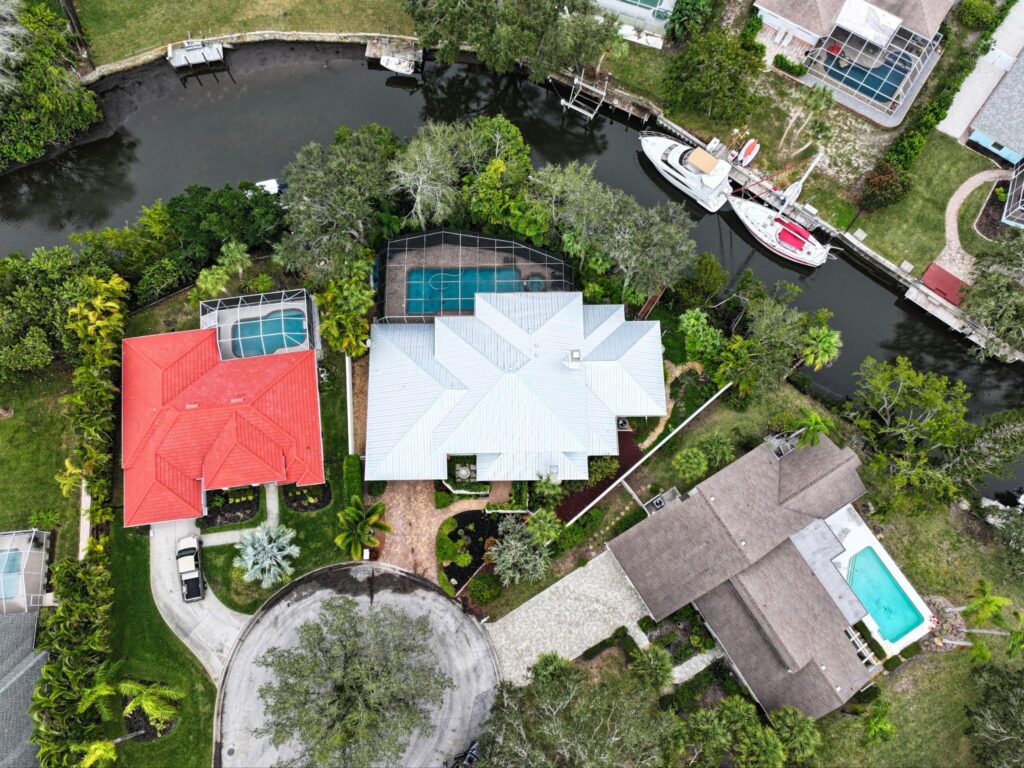 A high-altitude bird's-eye view of a coastal cul-de-sac and canal neighborhood showcasing a brilliant white Metal Roofing Bradenton FL home profile by Sunshine Metal Supply.