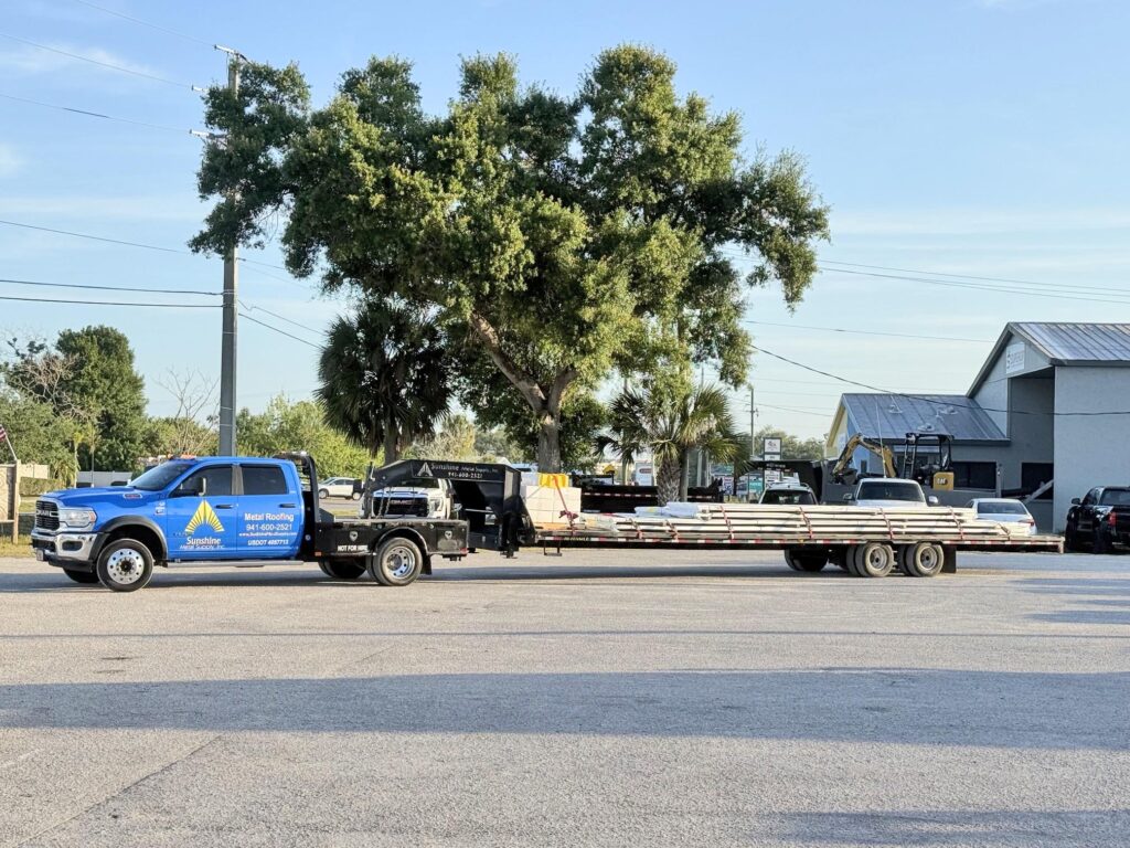 A blue Sunshine Metal Supply commercial transport truck and trailer loaded with custom-fabricated panels, delivering various Metal Roofing Types to a job site.