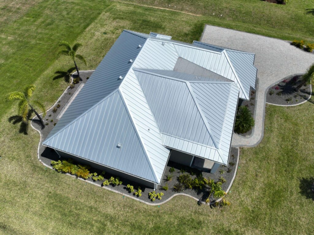 Direct aerial view of a modern residential hip roof clad in silver aluminum panels, showcasing an ideal system for Metal Roofing Naples FL by Sunshine Metal Supply.