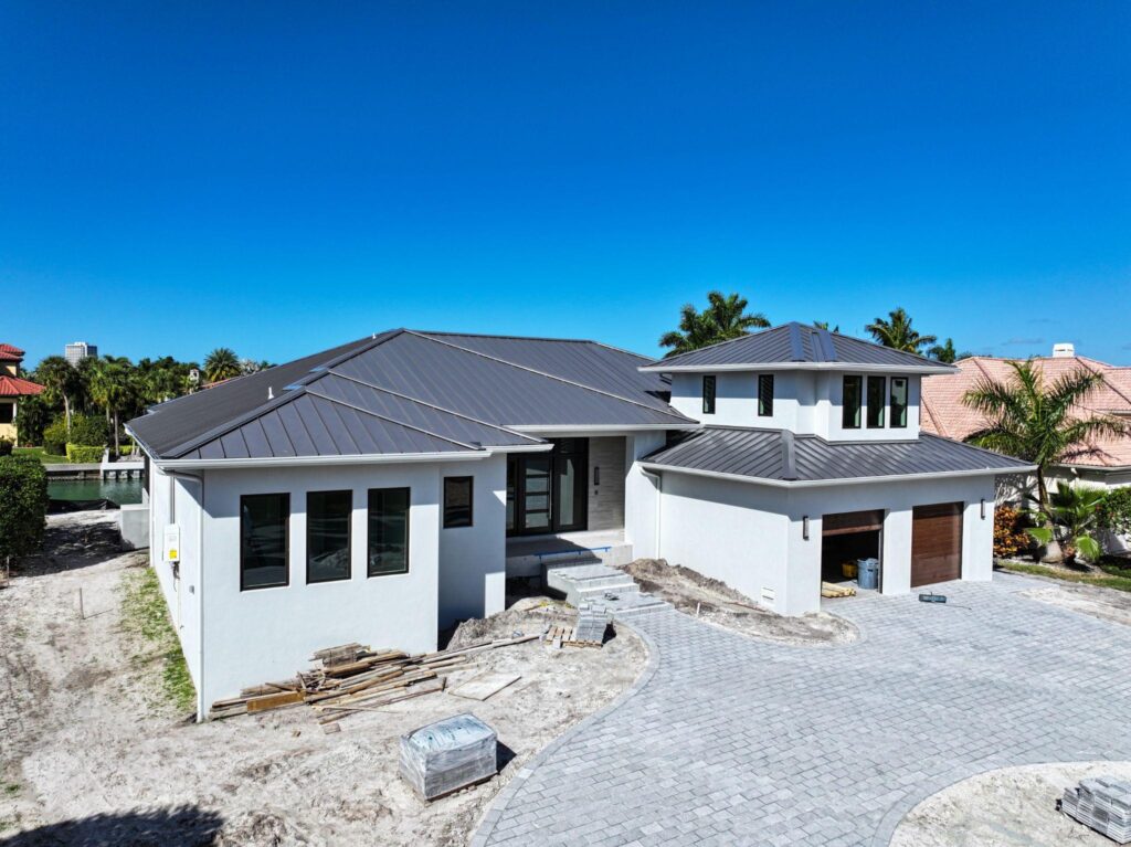 A modern coastal home with white stucco walls featuring a clean dark gray metal roof installed with a premium SUNLOC Standing Seam system by Sunshine Metal Supply.